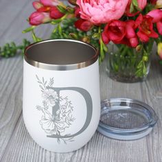 a white coffee mug with the letter d on it next to some flowers and a glass