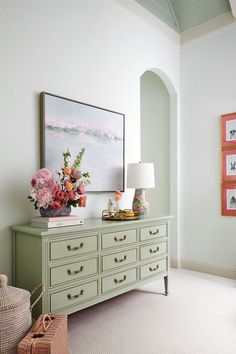 a green dresser with flowers on it in a white room next to a painting and lamp