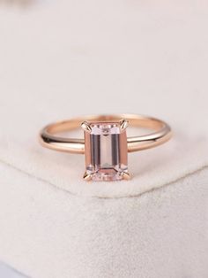 an engagement ring with a pink morganite stone in the center on a white cushion