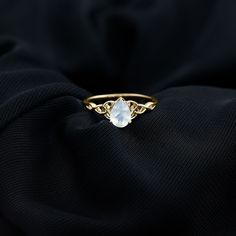 a gold ring with a white stone sitting on top of a black cloth in the dark