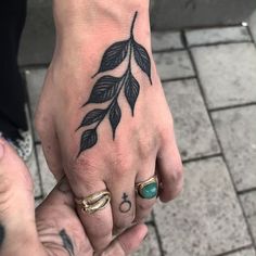 two people with tattoos on their hands holding each other's hand and one has a leaf tattoo on it