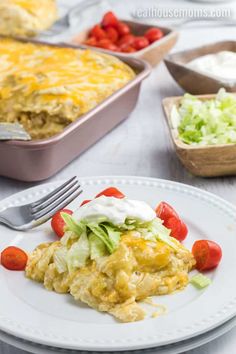 a white plate topped with an enchilada covered in lettuce and tomatoes