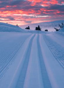 the sun is setting over some snow covered hills with tracks in the foreground and trees on the far side