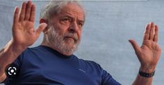 an older man with white hair and beard wearing a blue t - shirt holds his hands up in the air