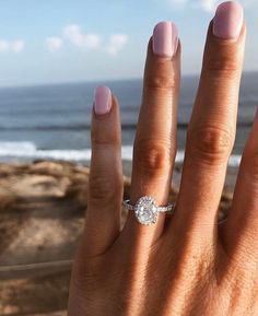 a woman's hand with a diamond ring on her finger near the ocean and sky