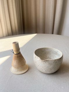 a white table with a small bowl on it and a vase sitting next to it