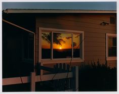 the sun is setting in front of a house