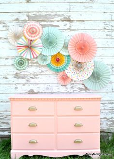 a pink dresser sitting in front of a wall with paper umbrellas on top of it