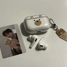 an apple airpods with a bear keychain attached to it, next to two other items