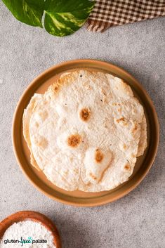 two tortillas on a plate next to a bowl of flour and a plant