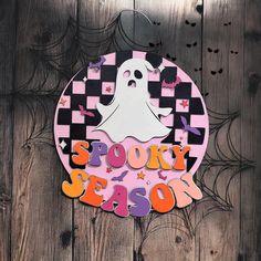 a sign that says spooky season with a ghost in the center on a wooden background