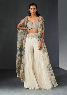 Editor's Note Presenting an exquisite ensemble: a champagne-blue cape that gracefully complements an ambi jaal embroidered bustier and an embroidered waist net sharara. This ensemble effortless... Sharara And Cape, Sangeet Outfit Sharara, Roce Ceremony Outfits, Indian Cape Outfits, Elegant Palazzo Set With Sheer Dupatta And Cape Sleeves, Georgette Sets With Cape Sleeves For Eid, Elegant Palazzo Set With Cape Sleeves For Diwali, Designer Palazzo Set With Cape Sleeves For Eid, Diwali Georgette Sets With Cape Sleeves