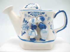 a blue and white porcelain teapot with two children on it's side, sitting on a table