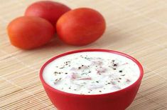 a red bowl filled with yogurt next to three tomatoes