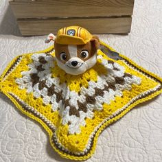 a crocheted blanket with a stuffed animal wearing a construction hat on top of it