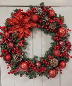 a christmas wreath with poinsettis and pine cones hanging on a white door