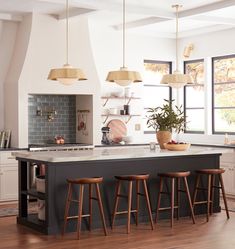 an island in the middle of a kitchen with stools and lights hanging above it