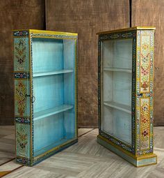 two blue and gold painted bookshelves sitting next to each other on a wooden floor