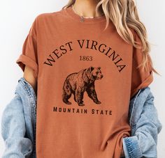 West Virginia Mountain State Tshirt, Black Bear Gift Tee The Comfort Colors C1717 100% Ring Spun Cotton T-Shirt is very appropriately-named. All colors are inspired by nature and have a perfect lived-in, weathered look. Shirts are sent through a unique dyeing process that makes them incredibly soft and long-lasting. Each piece is soft-washed 50 times before making its way to you! Stitched at the collar, armhole, sleeves and bottom hem for ultimate durability, you will notice the density and qual Bear Tshirt Design, Nature Graphic Tees, West Virginia Mountains, Perfect Live, Lifestyle Clothing, Dyeing Process, Life Design, Black Bear, Look Plus