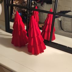 three red christmas trees sitting on top of a white counter next to a black framed mirror