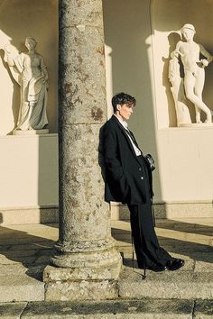 a man in a suit and tie leaning against a pillar