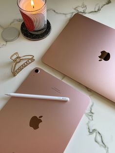 two apple laptops sitting on top of a table next to a candle and pen