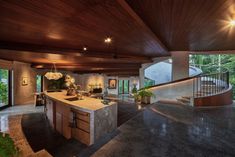 an open kitchen and living room with stairs leading to the upper floor, surrounded by greenery