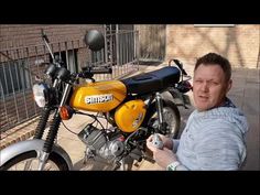 a man sitting next to a yellow and black motorbike in front of a building