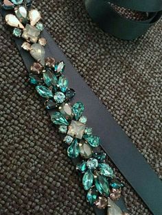 a black belt with blue and green jeweled stones on it, next to a roll of ribbon