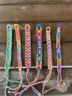 five different colored bracelets are lined up on a wooden surface and one is tied to a string