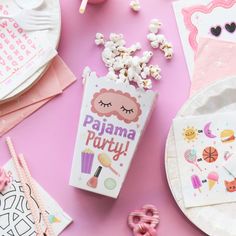 a pink table topped with lots of candy and other items next to a box of popcorn