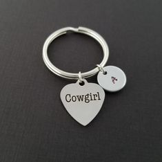 a heart shaped keychain with the word cowgirl written on it and two charms attached