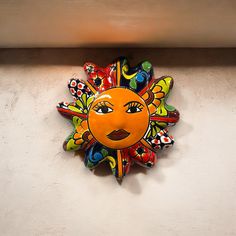 a colorful sun decoration on the side of a white wall with an orange and yellow face