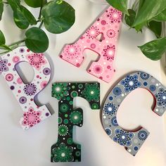 three colorful wooden letters sitting on top of a white table next to green leaves and flowers