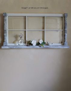 an old window frame with flowers and candles in it is hung on the wall above a bed