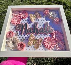 a person holding up a shadow box with flowers and butterflies on it in the grass