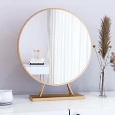 a round mirror sitting on top of a white table next to a vase with flowers