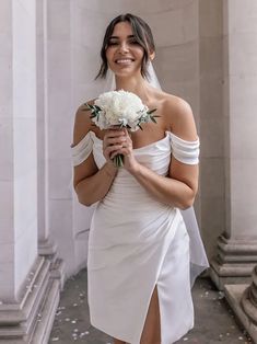 a woman in a white dress holding a bouquet of flowers and posing for the camera