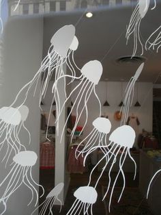 some white jellyfish are floating in the water and hanging from wires on a wall