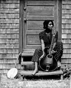 a woman sitting on steps holding a guitar in front of a wooden door with her legs crossed