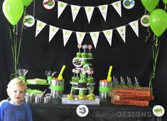 a little boy standing in front of a table filled with green and white balloons, cake and cupcakes