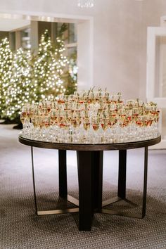 a table full of champagne glasses on top of a round table in front of a christmas tree