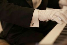 a man in a tuxedo and white gloves plays the piano with his hands