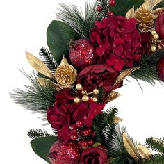 a christmas wreath with red flowers and greenery on it's side, surrounded by golden ornaments