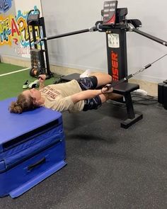 a woman laying on top of a blue bench next to a gym equipment set up