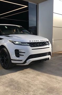 a white range rover parked in front of a garage with its door open to reveal the new car