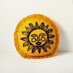 a yellow pillow with a sun design on it's face and fringes around the edges