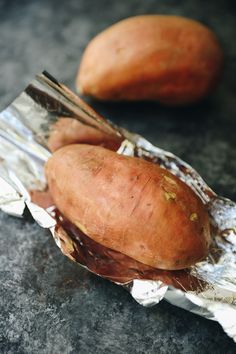 two sweet potatoes wrapped in foil on a table