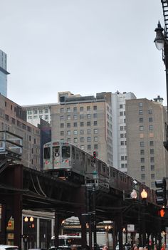 a train traveling over a bridge in the middle of a city with tall buildings behind it