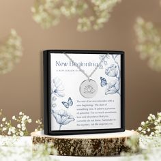 a new beginning necklace in a box on a tree stump with flowers and butterflies around it